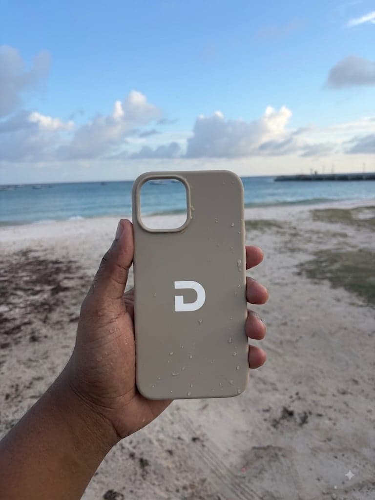 A hand holding the tan Dap case, still wet from the ocean, on the beach